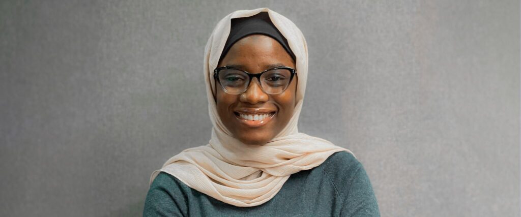 Woman wearing a white hijab and black to clear ombre glasses smiling