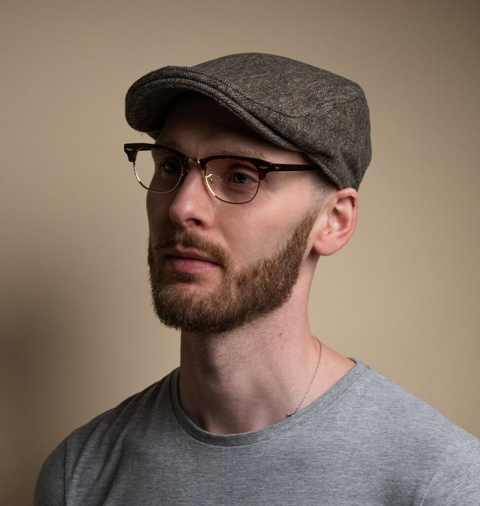 Man posing with a baker boy hat wearing clubmaster frames looking to the left