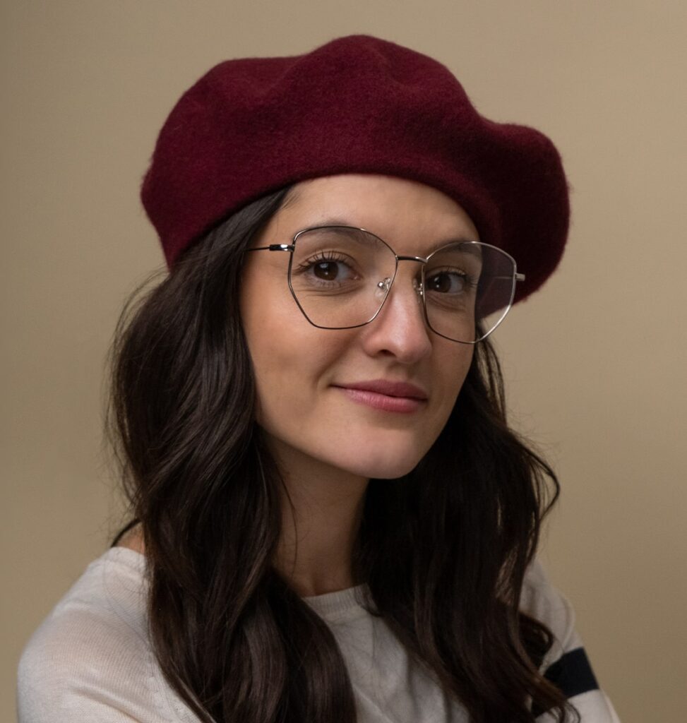 Woman wearing a red beret hat and oversized metal frames looking at camera