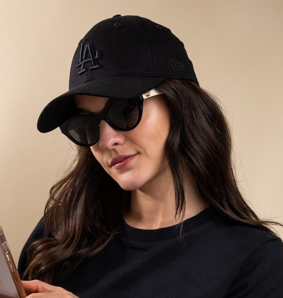 Woman wearing a pair of sunglasses and black baseball cap looking at her phone