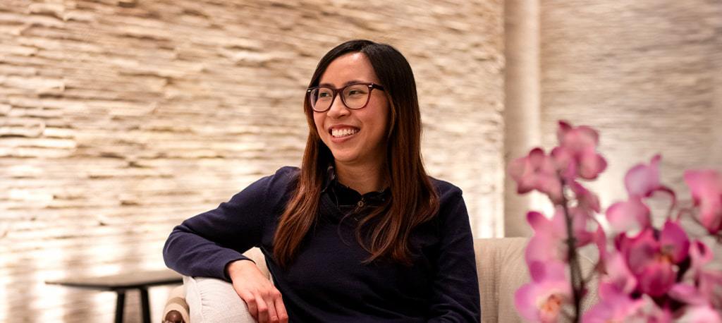 Candy from Glasses Direct smiling while sitting on a sofa next to some flowers