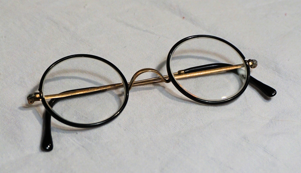 A vintage pair of round metal glasses folded on a smooth surface