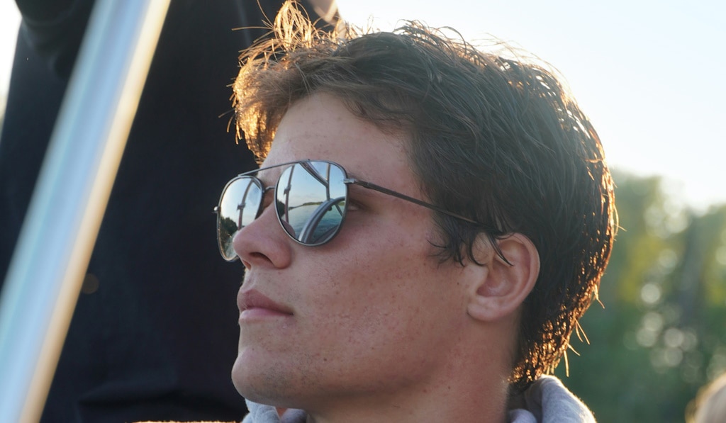 A young man with tousled hair wearing mirrored aviator sunglasses while looking thoughtfully into the distance