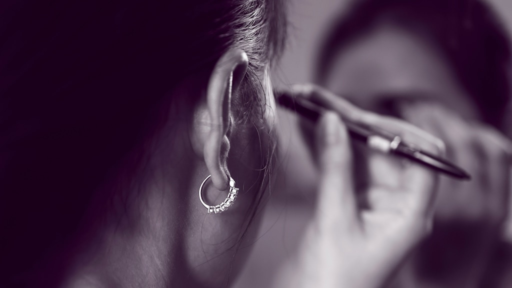 Slightly blurry greyscale photo of the side of a woman's head as she raises a brush to apply make-up to her brows