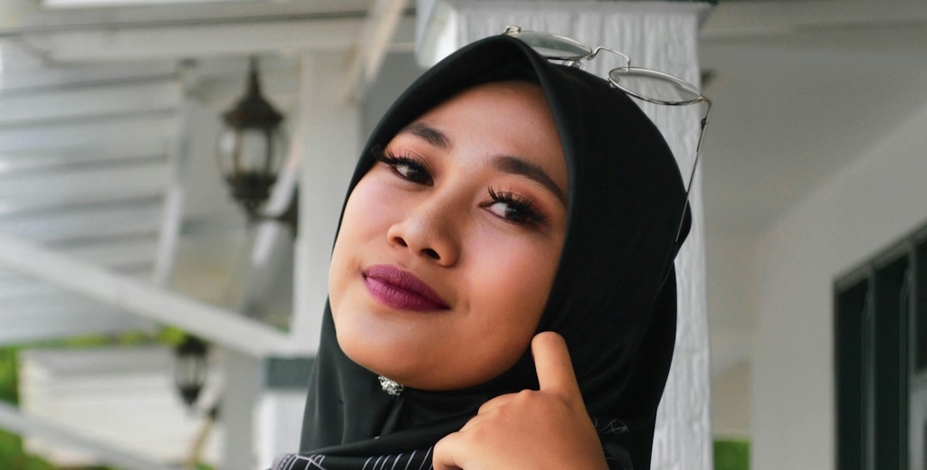 A woman wearing a hijab and glasses on her head, with her make-up drawing attention to her striking dark eyes