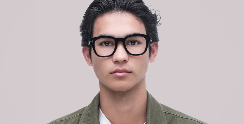 A young man with swept-back black hair wearing thick black acetate frames with square lenses