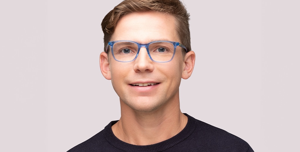 A man with short blond hair smiles while wearing transparent light blue frames with square lenses