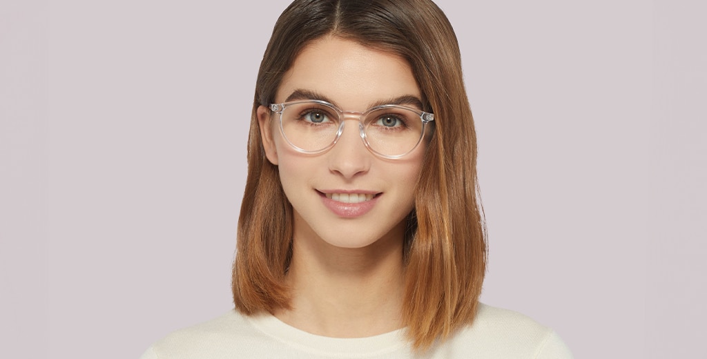 A woman with light brown, medium-length hair smiles while wearing transparent round acetate frames