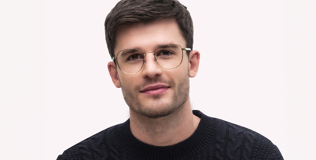 A man with short brown hair and slight stubble on his face wears square but slightly rounded gold metal frames