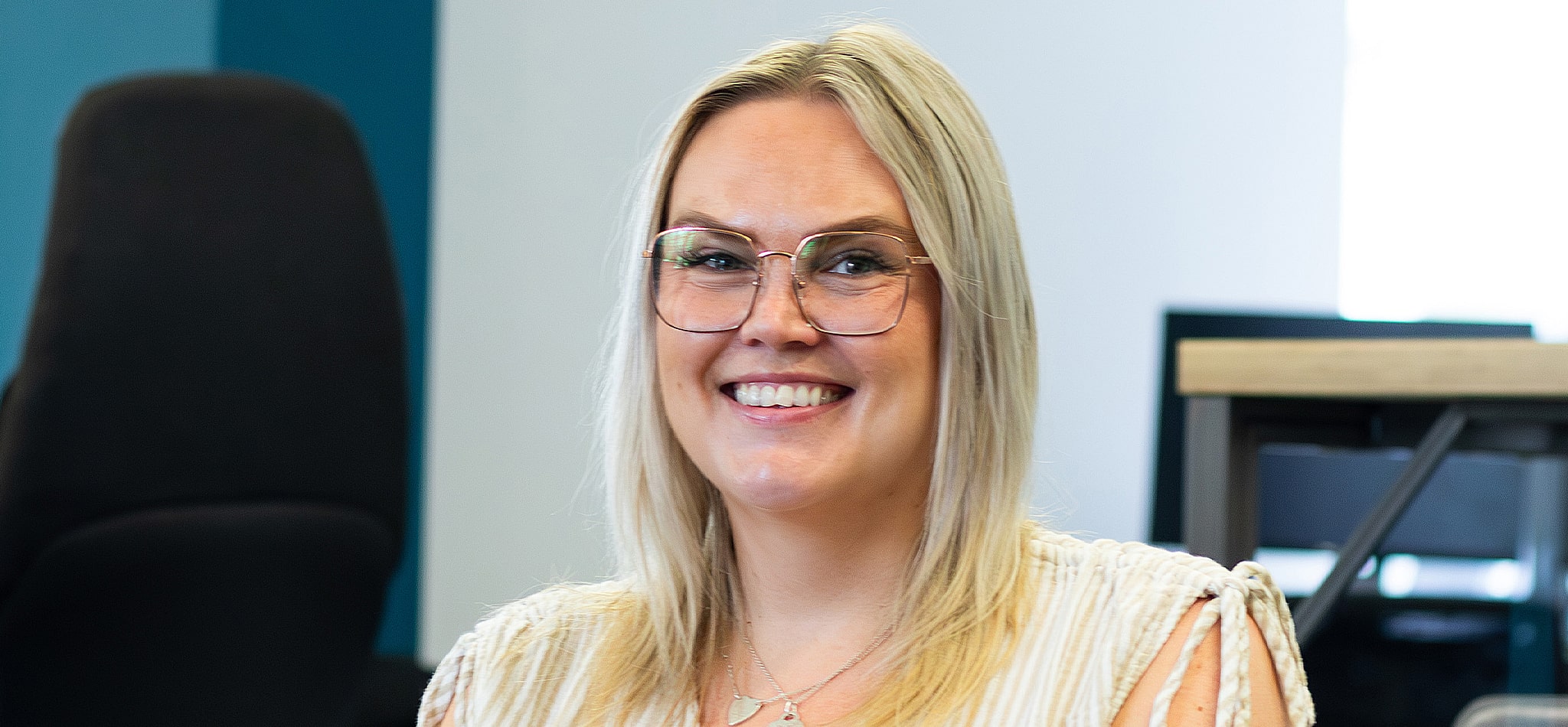 A woman with shoulder-length bright blonde hair smiles while wearing large square metal glasses