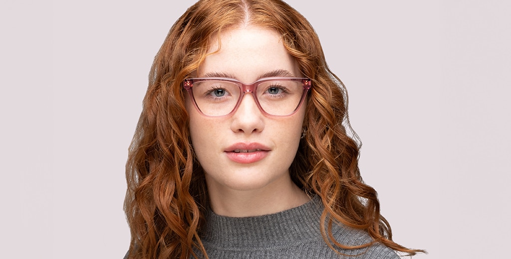 A woman with long red wavy hair wearing transparent pink cat-eye glasses