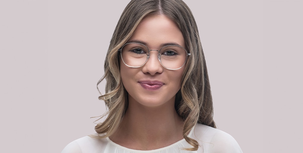 A woman with long brown hair with blonde highlights smiles while wearing large round silver frames