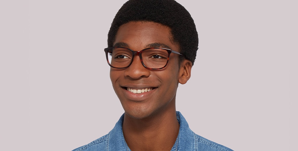 A man with short, curly black hair smiling brightly in his square tortoiseshell glasses