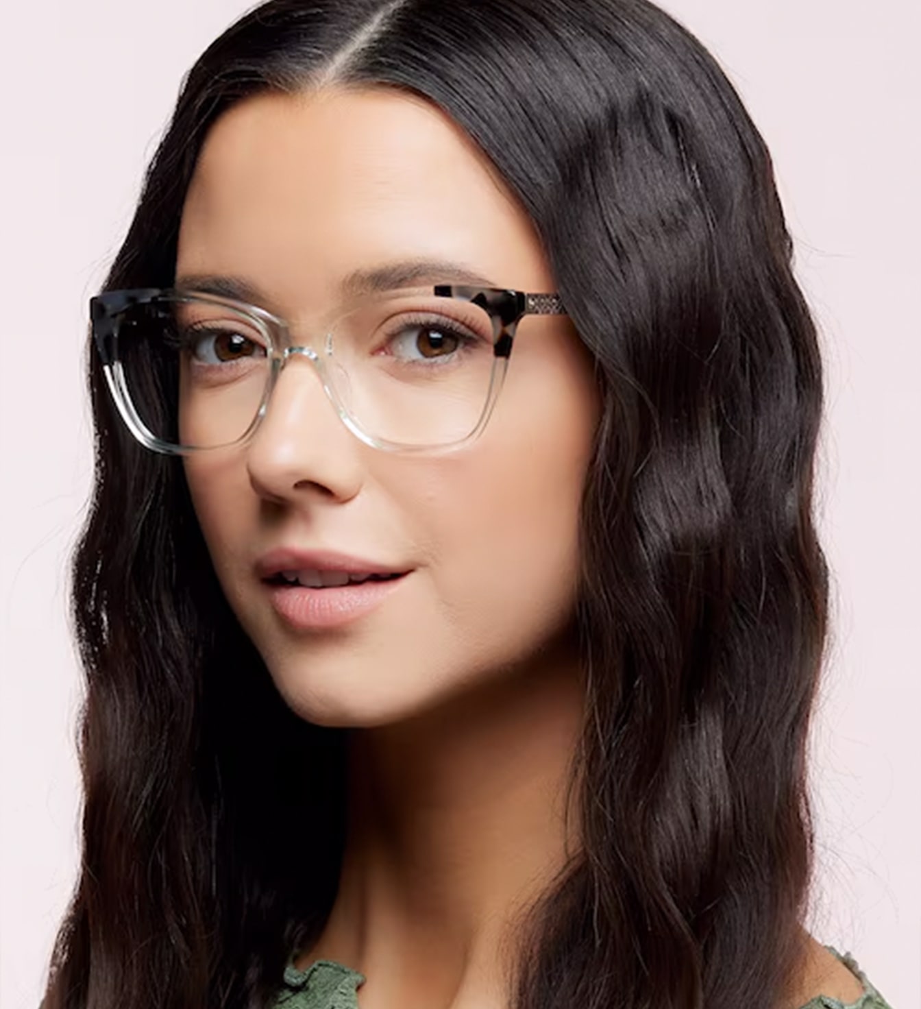 A young lady with dark wavy hair is wearing a transparent cat-eye frame with tortoise print along the top of the design.