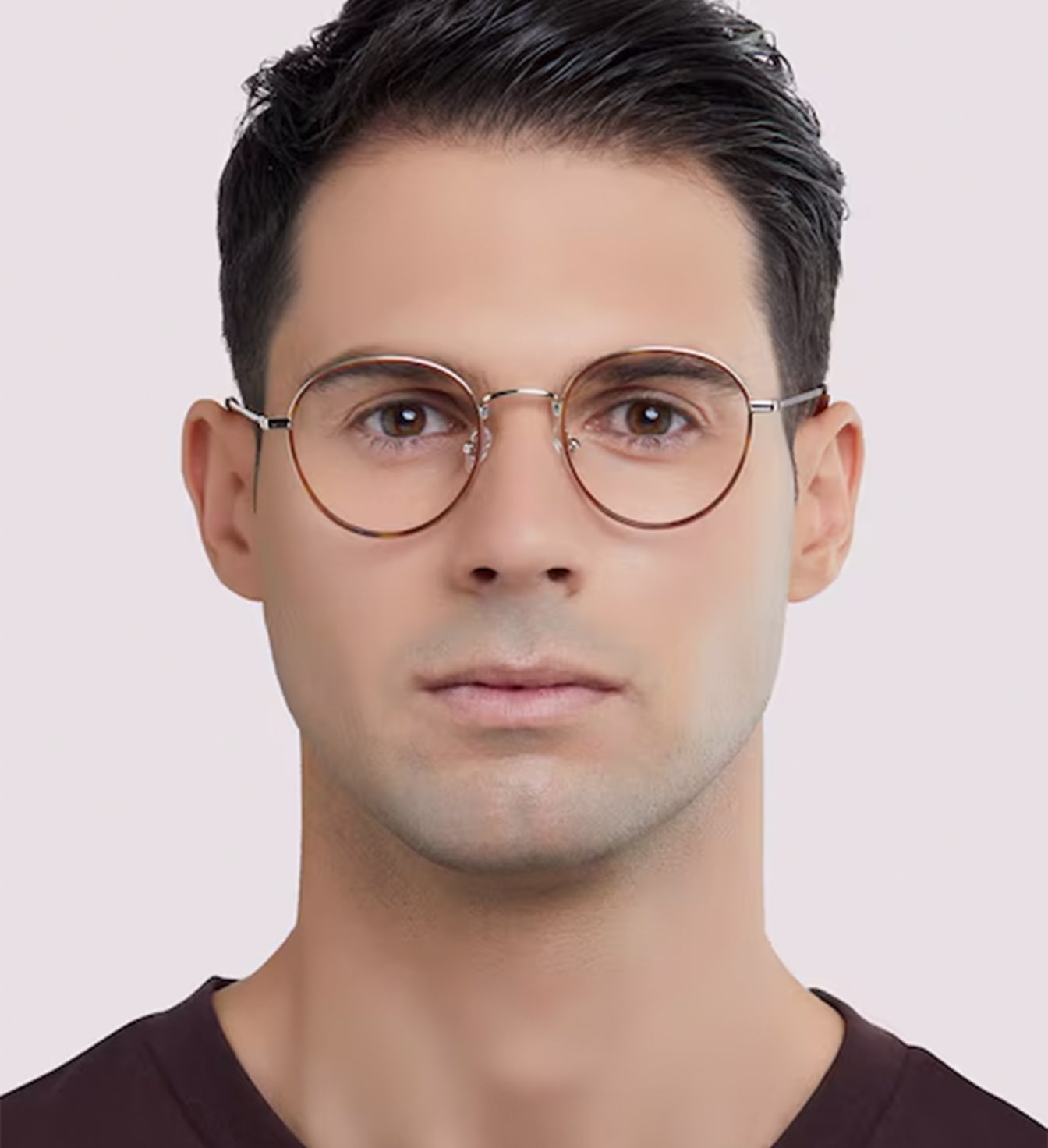 A young man with short dark-brown hair swept back. He is wearing a retro-style pair of metal round glasses and a dark t-shirt. 