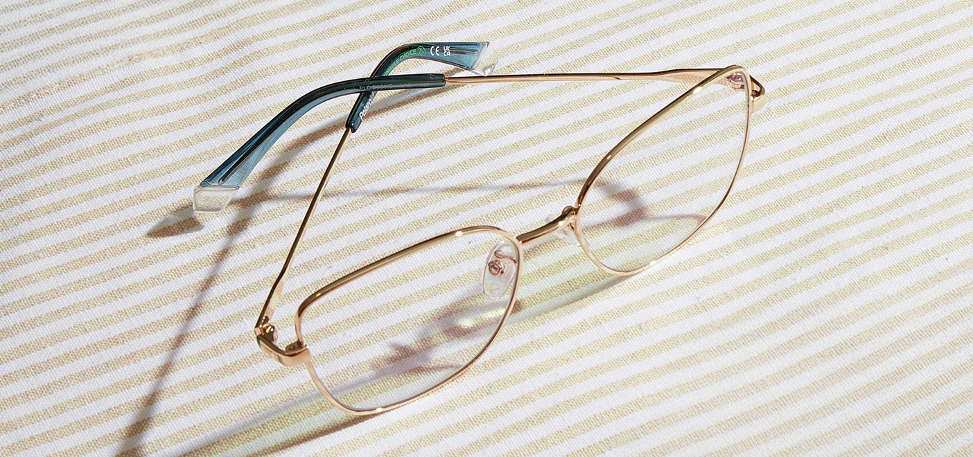 Large metal butterfly glasses with green accents resting part-closed on a beige and white picnic blanket. 