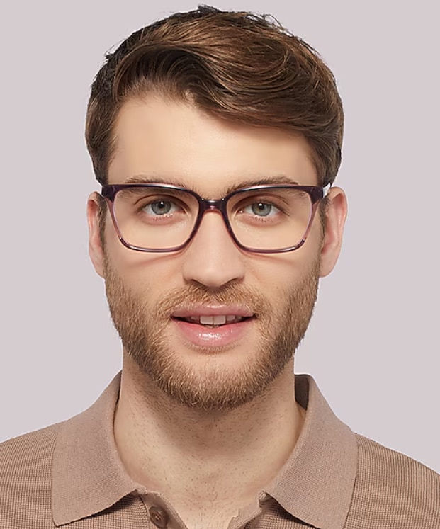 Close-up of a man wearing purple rectangular glasses, with short strawberry-blonde hair and a trimmed beard, against a plain background.