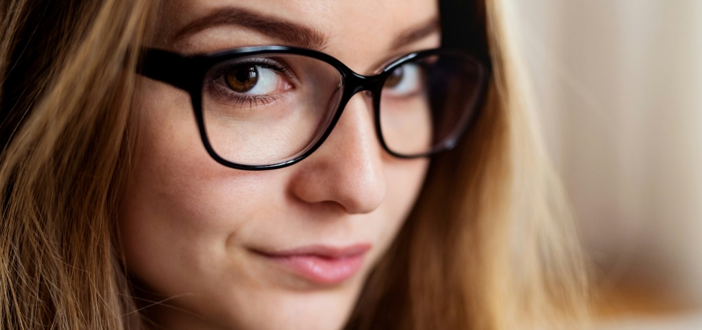 A close up of a young lady with blonde hair and brown eyes. She is wearing a pair of black acetate glasses which are sitting comfortably on her nose. 