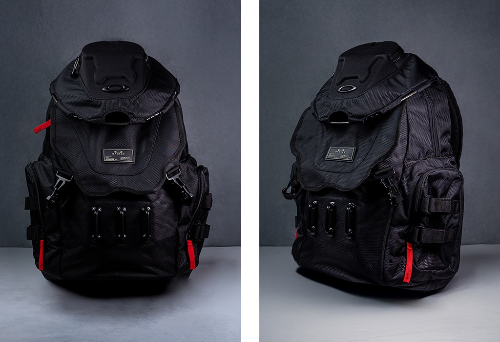 Two portrait images side-by-side of a black Oakley backpack on a grey background. It is large, has several pockets and three red zips. The Oakley 'O' symbol is on the top and a branded badge is attached to the middle.