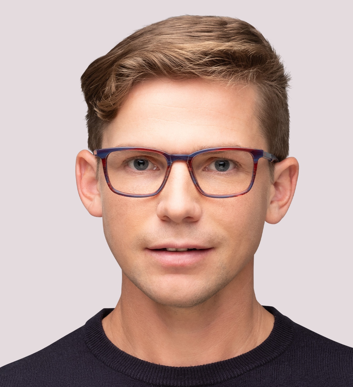 A close up of a young man with short blonde hair. He is wearing a pair of red stripy New Balance glasses and a navy sweater.