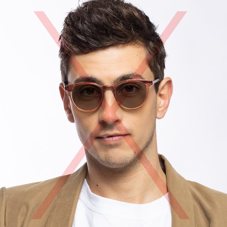 A cropped headshot of a young man with brown hair wearing a pair of red sunglasses, a white t-shirt and brown blazer. There is a red cross through the image to indicate that it's not an appropriate passport photo.