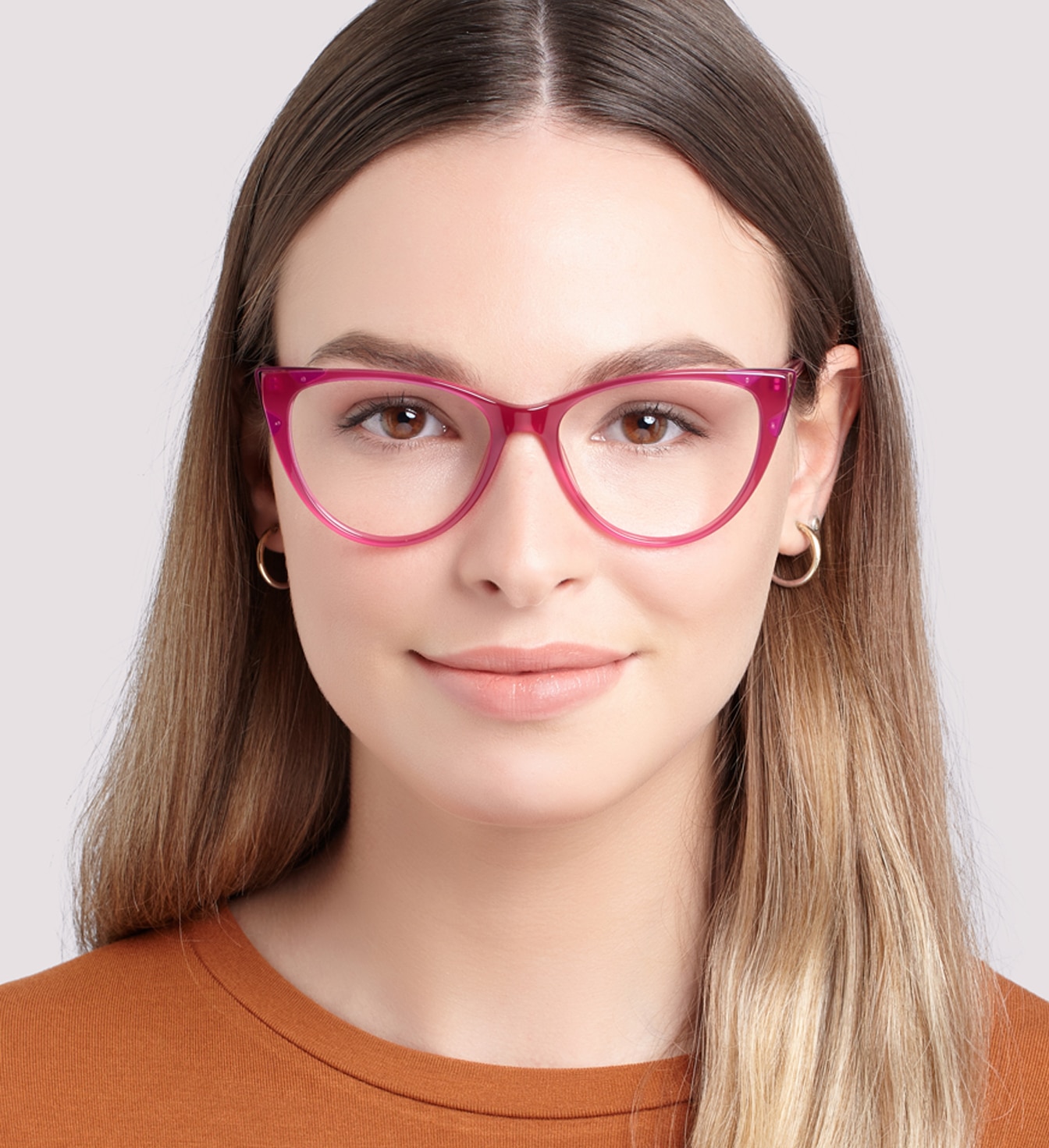 A close up of a young lady with long blonde hair and brown eyes. She is wearing bright pink cat-eye glasses, gold hoop earrings and an orange t-shirt.
