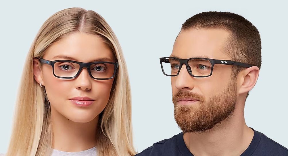 A man with a short beard wearing black Oakley® Hex Jector rectangular glasses, and a woman with long blonde hair wearing black Oakley® Plank 2.0 glasses, both against a plain white background.