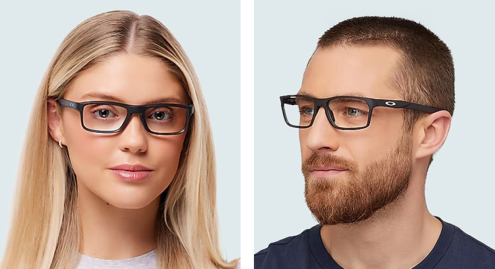 A young woman and man pose against a grey-white backdrop. The woman, with long blonde hair and dark eyes, wears a white t-shirt and rectangular Oakley glasses. Beside her, the man—sporting cropped blonde hair, a neat beard, and a dark-blue t-shirt—faces slightly to his right, toward the woman, also wearing rectangular Oakley glasses.