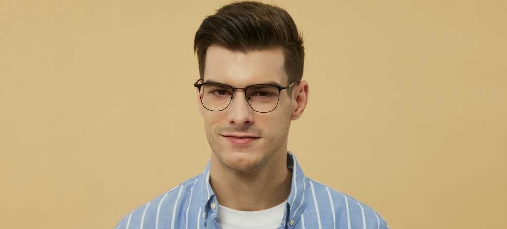 A young man with brown hair and a quiff, he is wearing a pair of black titanium glasses and a blue-and-white striped shirt. The background is a golden yellow. 
