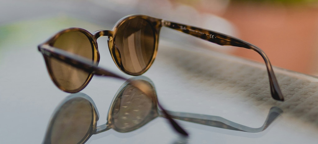 A pair of round acetate sunglasses lying open on a table, facing away from the camera.