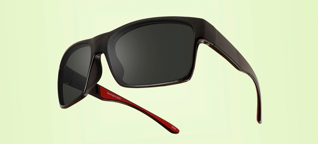 A black pair of square acetate sports sunglasses with bright-red rubber inserts along the temples. They are suspended mid-air on a light-green background. 