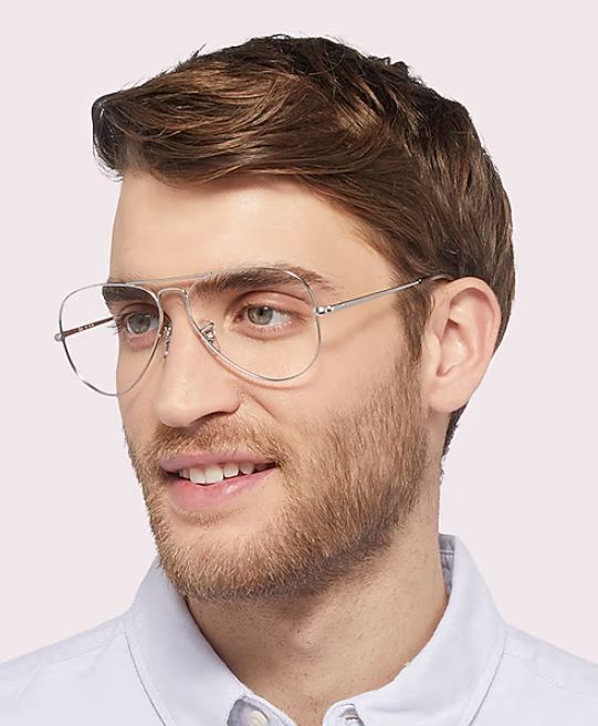 A portrait of a young man with short, blonde hair against a white background. He’s wearing Ray-Ban aviator glasses and a white-collar shirt, gazing off to the far right.
