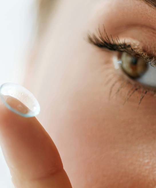 A close-up of a woman placing a contact lens onto her eye with her fingertip.