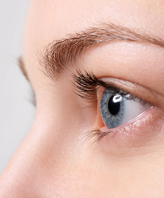 A side close-up of a woman's blue eye in a brightly lit setting.