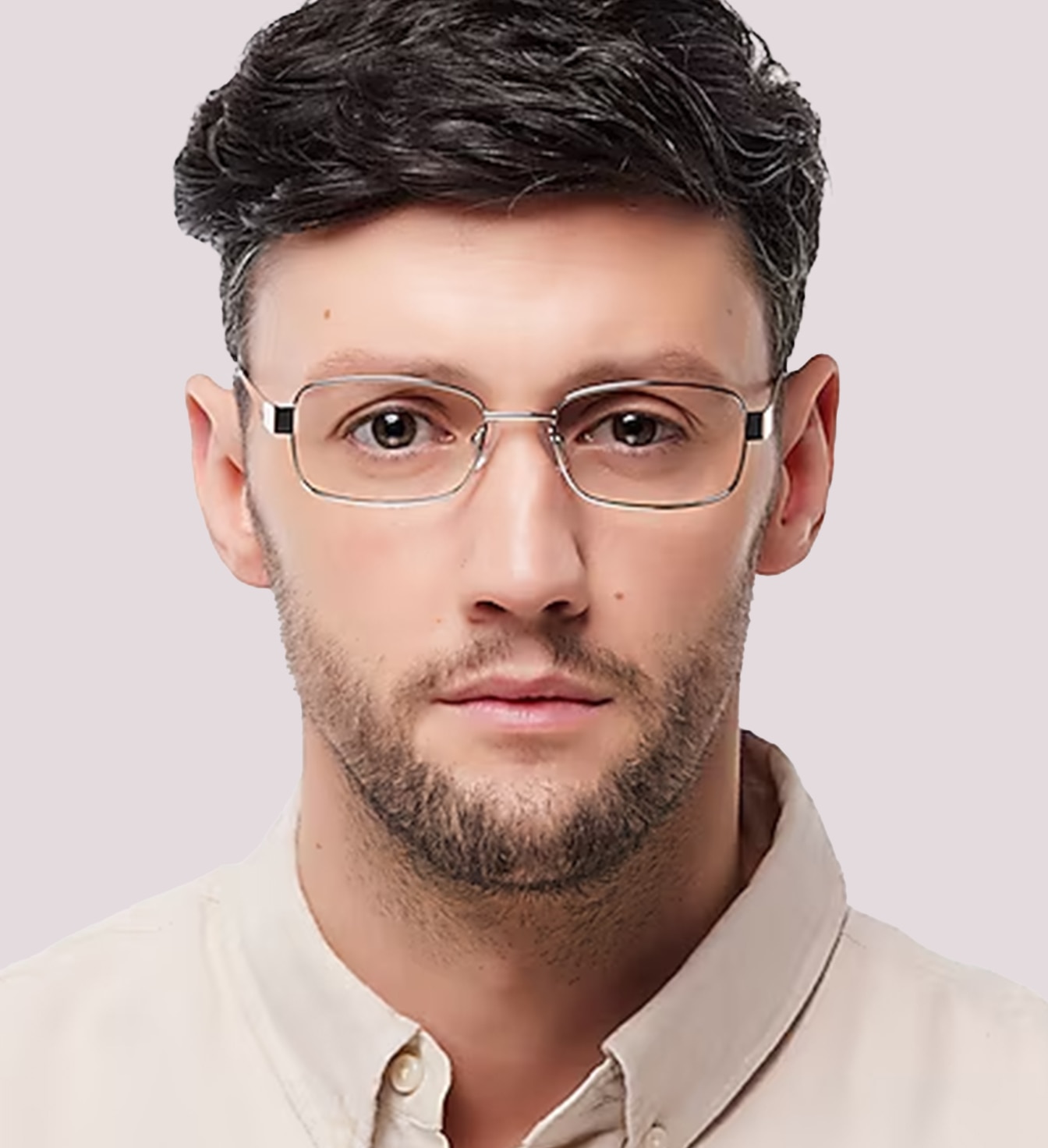 A close-up portrait of a man facing forward with a salt-and-pepper quiff, wearing silver metal rectangular glasses and a cream shirt against a plain background.