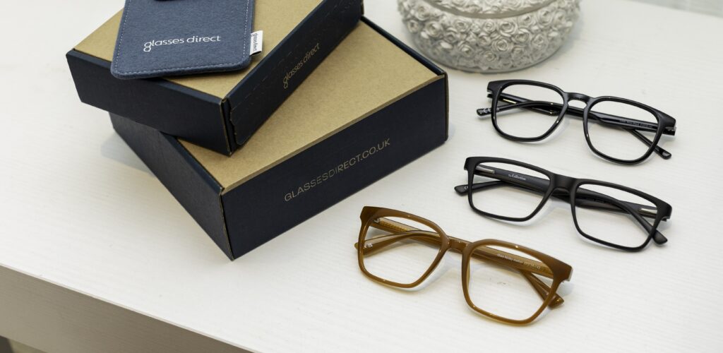 Three glasses frames on a white table next to Glasses Direct boxes and a soft glasses case.