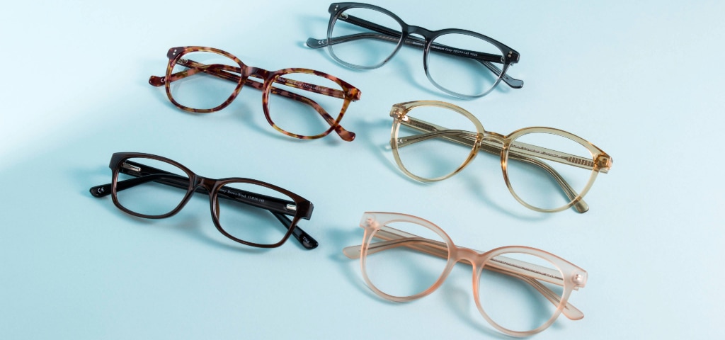 Five pairs of prescription glasses in different acetate frame styles and colours arranged on a light blue background.