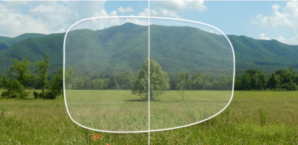 A scenic landscape of a grassy field with trees and mountains in the background, overlaid with a lens-shaped outline split down the middle. The left side appears smudged with fingerprints, while the right side is clear and sharp, illustrating how an oleophobic coating improves lens clarity by reducing smudges.