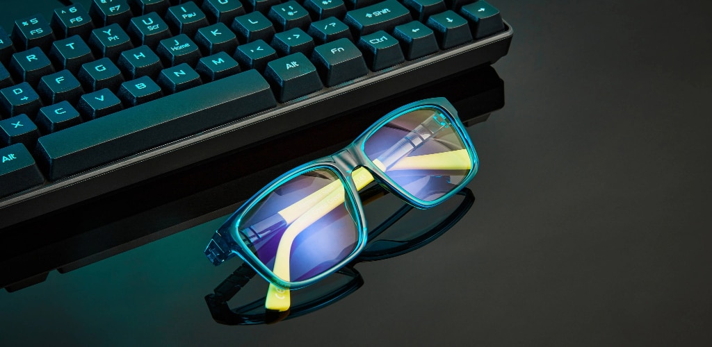 Blue light glasses placed beside a keyboard, showing reflective lenses designed to reduce glare from digital screens
