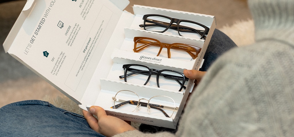 A person holding an open Glasses Direct Home Trial box with four frames laid out, showing different styles ready to try at home.