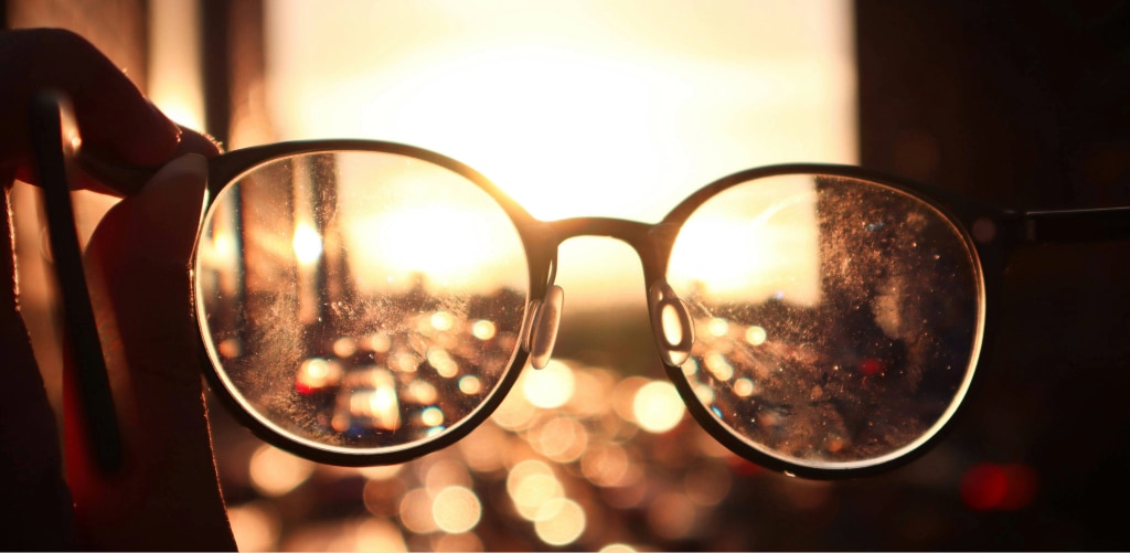 Close-up of dirty, scratched eyeglass lenses with sunlight glare, showing reduced clarity and visibility.