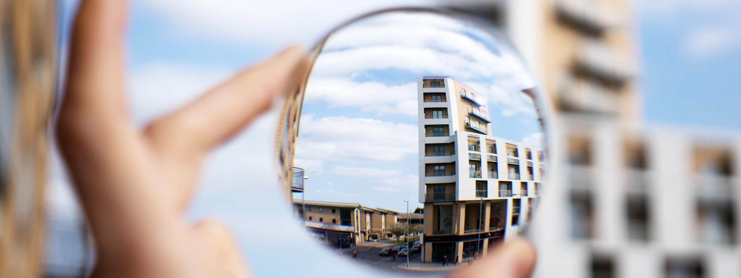 A close-up view through a glasses lens showing a building in sharp focus, while the surrounding area outside the lens appears blurred, illustrating corrected vision.