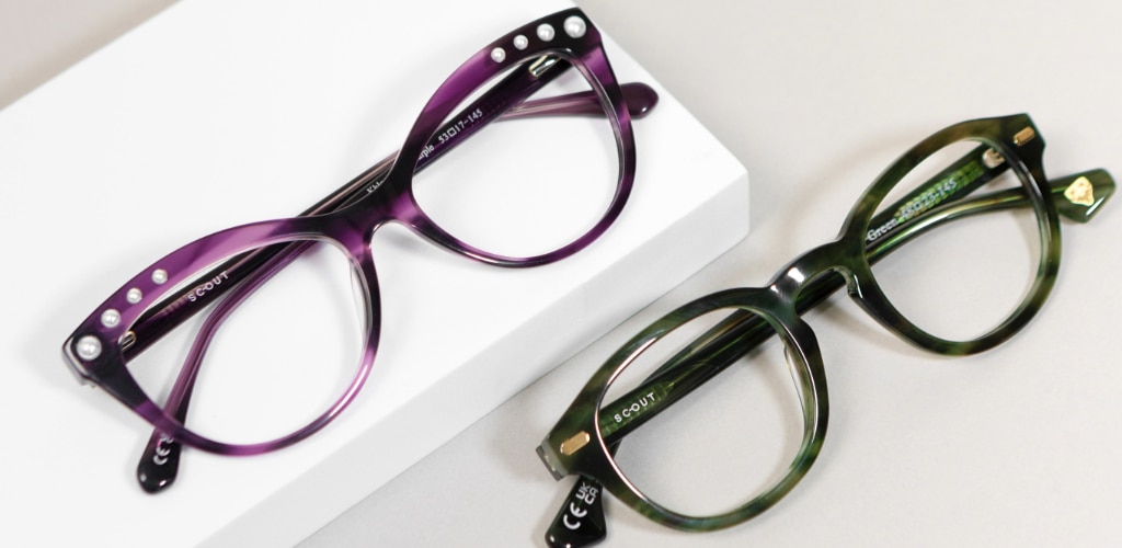 Two colourful acetate glasses frames displayed on a clean white surface, featuring rich tortoiseshell finishes. One frame is a bold purple cat-eye design with subtle pearl detailing along the temples, while the other is a striking green square frame with a modern, structured silhouette.