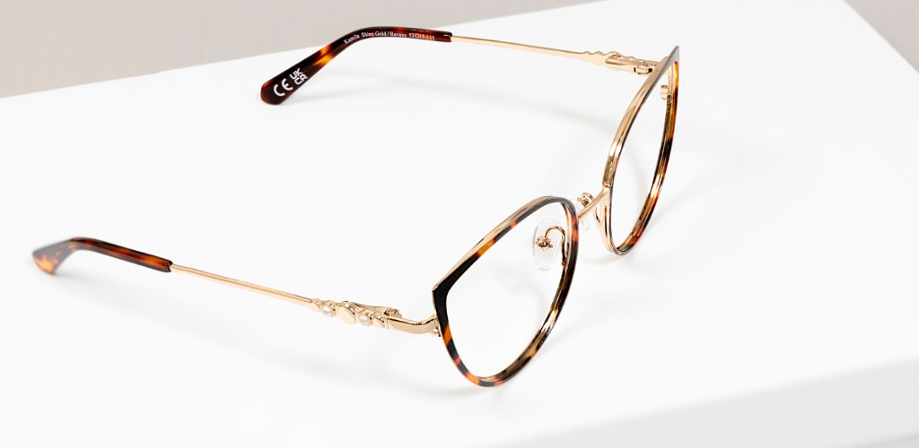 Close-up of gold metal cat-eye glasses with tortoiseshell detailing and adjustable nose pads on a white surface.