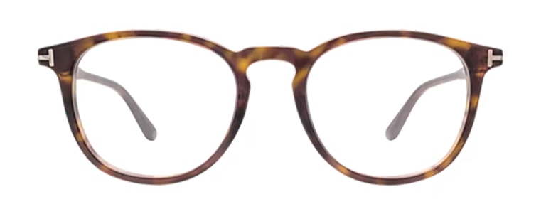 Front view of Tom Ford tortoiseshell glasses with softly rounded lenses and a keyhole bridge. The frames feature a subtle mix of brown, amber and dark tones. The glasses feature the iconic metal T design along the temples and are shown against a plain light background.