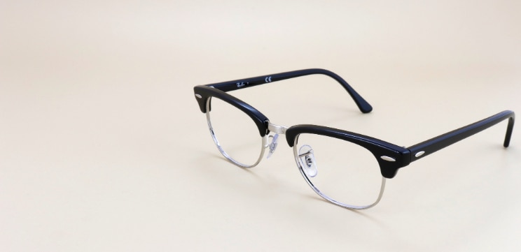 Ray-Ban® browline glasses in black with silver metal lower rims and pin accents, displayed against a warm neutral background.