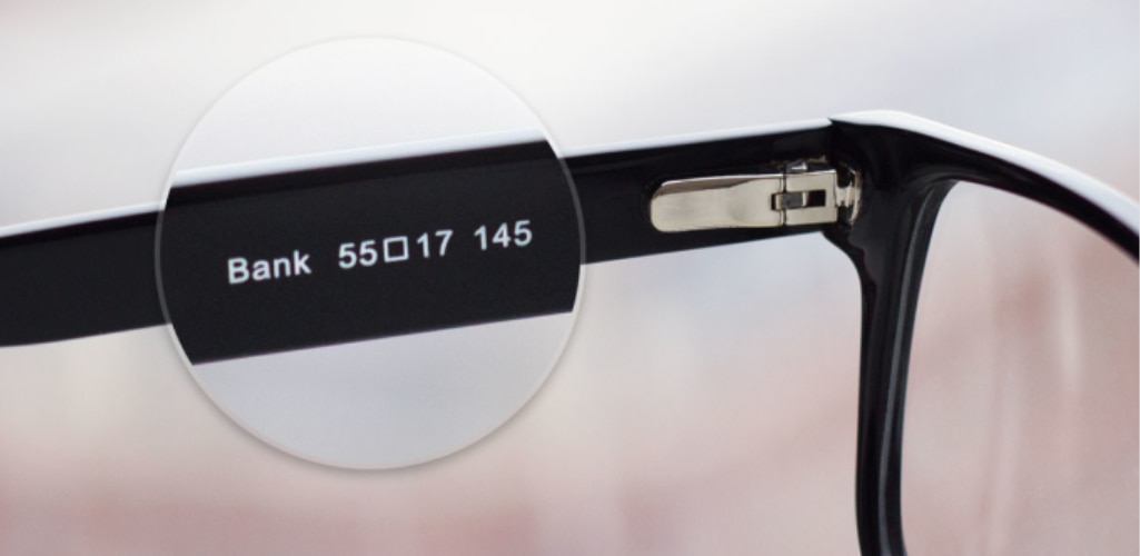 Close-up of the inside arm of a glasses frame showing frame measurements, including lens width, bridge width, and temple length, highlighted through a magnified view.