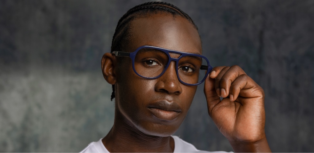 A man with neat braids wearing GD Maxwell bold deep navy pilot glasses adjusts the frames while looking towards the camera, showcasing their rich ink-blue colour and bold, modern design.