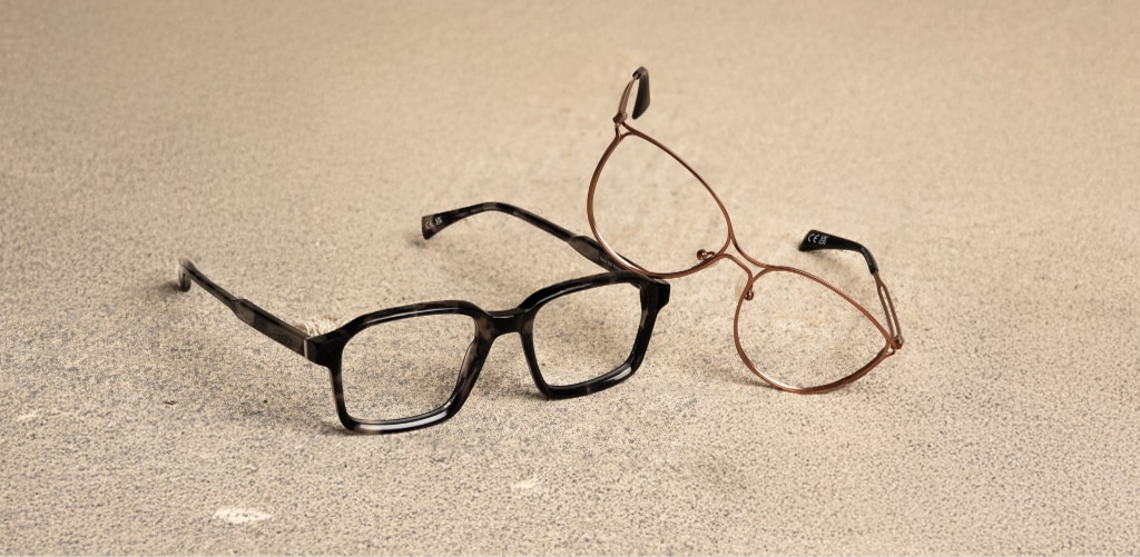 Two pairs of Scout glasses rest on a textured stone surface: Scout Martie, a bold rectangular acetate frame in Havana grey, and Scout Marine, a gold metal cat-eye frame. Together, they showcase cool-toned eyewear with contemporary, autumn-inspired finishes.