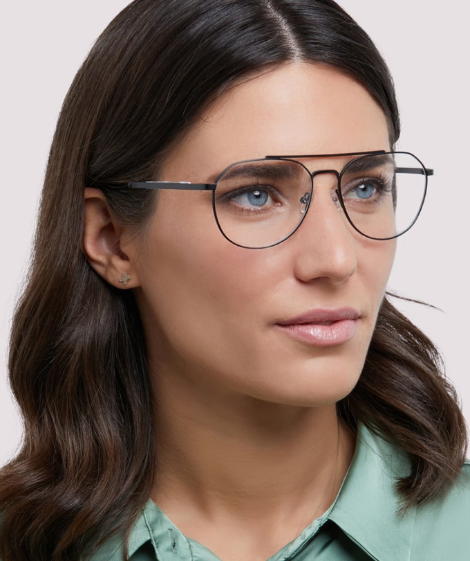 A woman with dark hair wearing a light green blouse and The Collection Colby large aviator black metal glasses.
